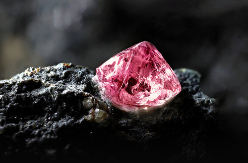Argyle Pink diamond rough cut on the surface of a black rock