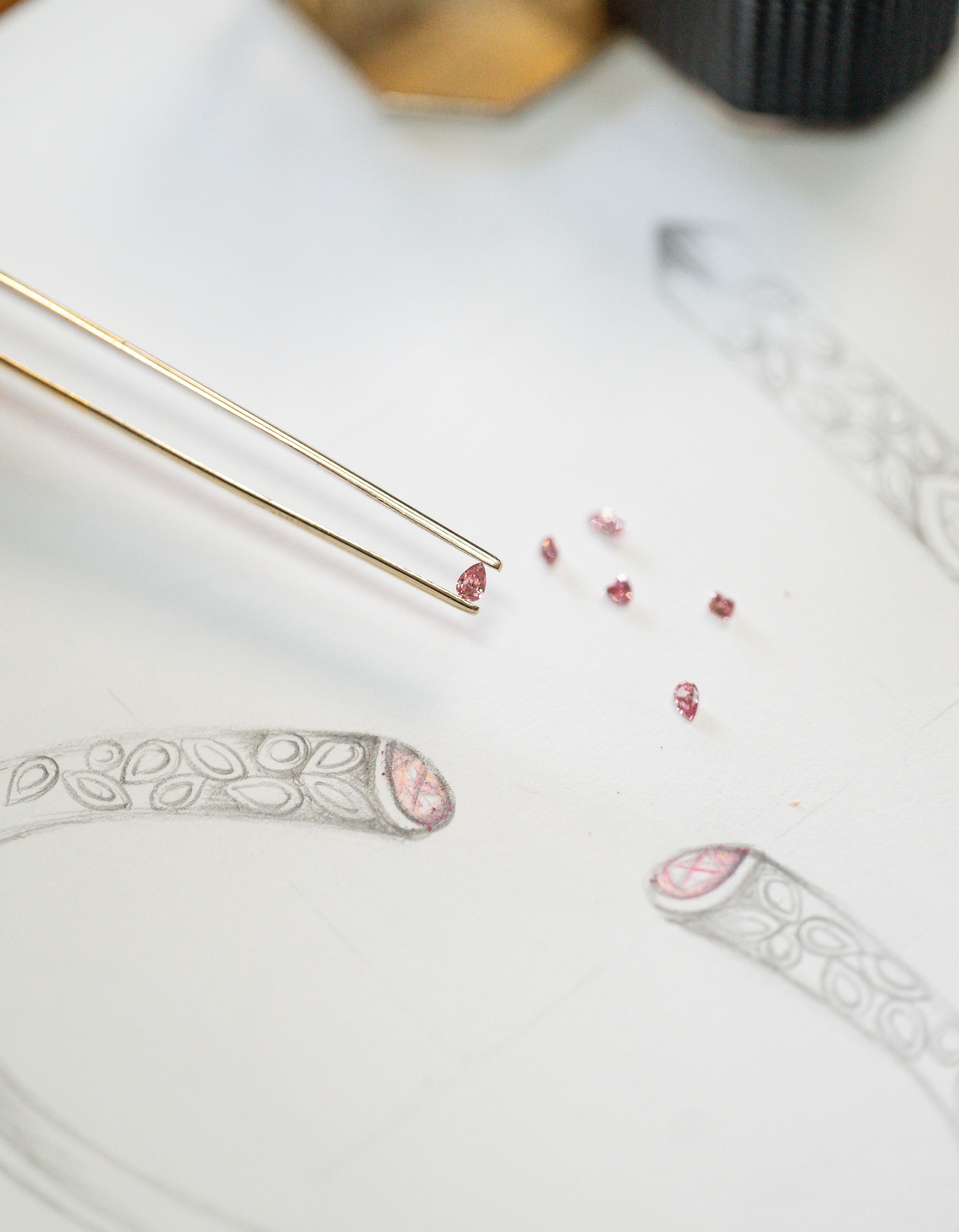 a number of pink Argyle diamonds scattered over an artist sketch of a jewellery design