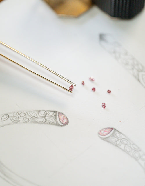 a number of pink Argyle diamonds scattered over an artist sketch of a jewellery design