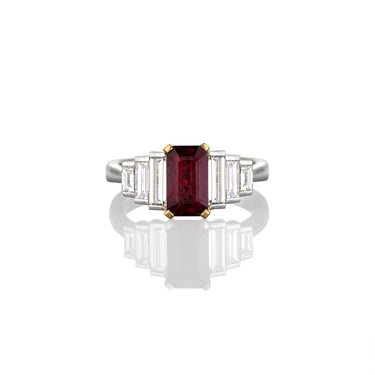 Ring with a central ruby gemstone flanked by emerald cut white diamonds on a white background