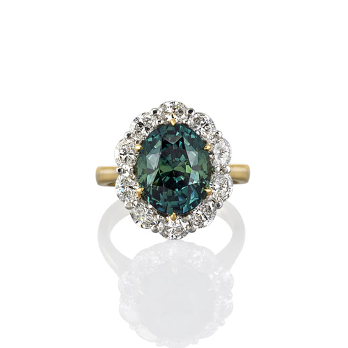 Yellow gold dress ring with central green halo sapphire. Smaller white diamonds surround the central stone. Shown here from above.