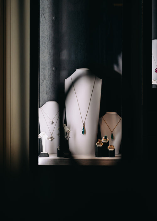 A display window showcasing several necklaces and earrings on white mannequin busts inside a dark shop display case.