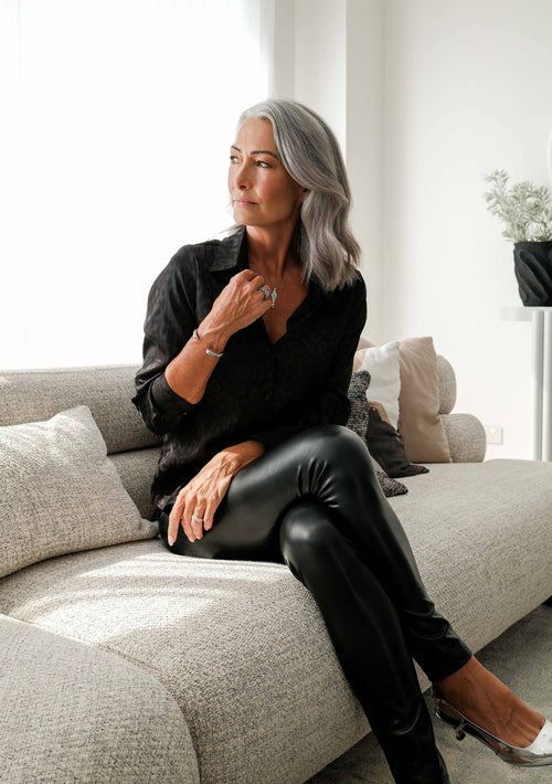 Woman sitting on a grey sofa in a modern living room her hand is touching her diamond white gold necklace.