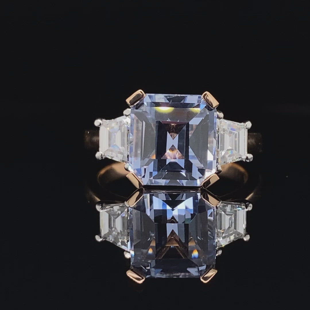 Video of the Trilogy square cut blue sapphire engagement ring with diamonds on rose gold band by Mondial by Nadia with a reflection underneath the ring.